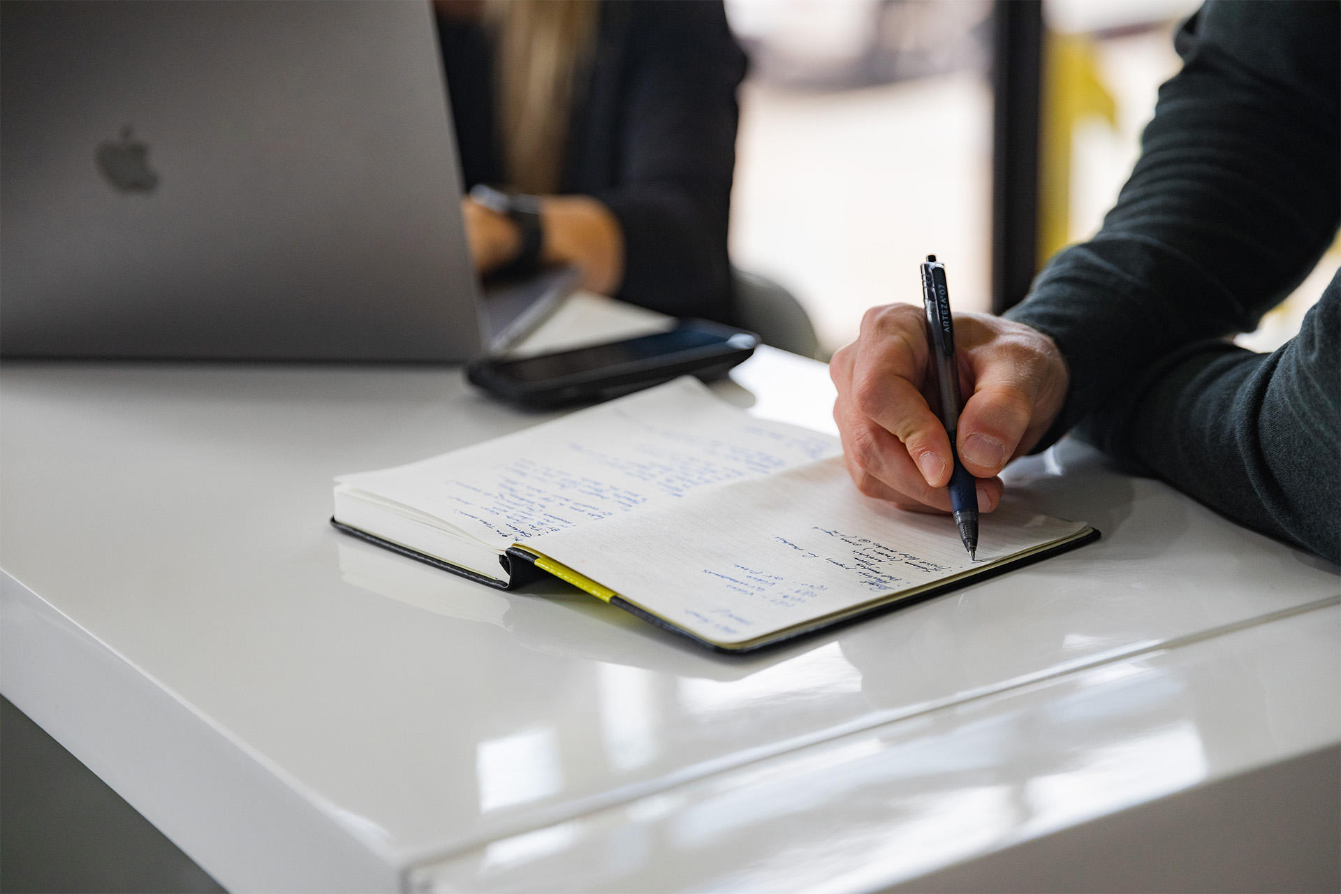 Man writing notes and women typing at a computer to create a video marketing plan. 